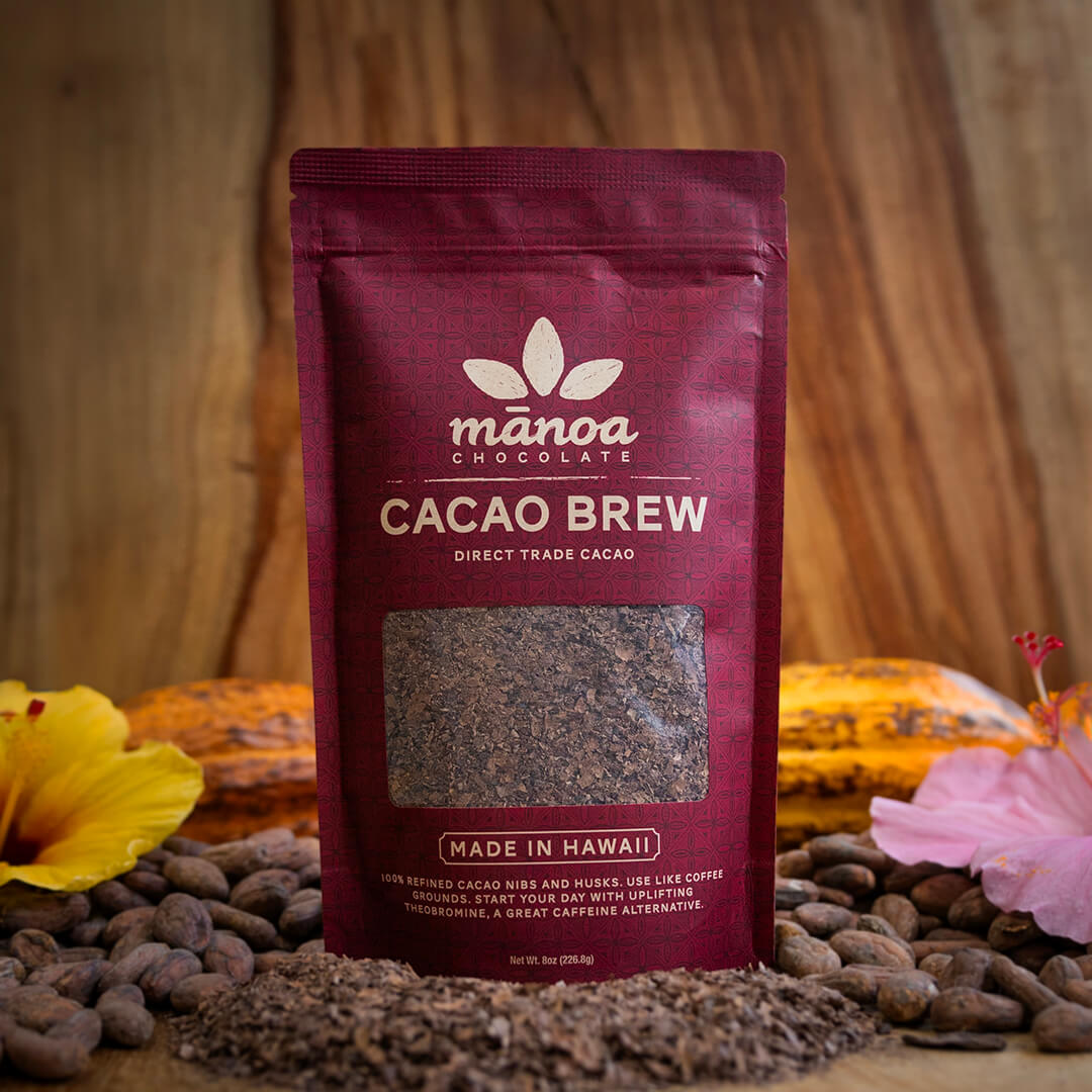 Image of an 8oz bag of Cacao Brew with cacao brew, cacao beans, tropical flowers and cacao pods on a wooden table