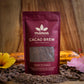 Image of an 8oz bag of Cacao Brew with cacao brew, cacao beans, tropical flowers and cacao pods on a wooden table
