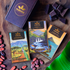 Image of kamananui, honolii, and kahaluu chocolate bar packages on a wooden table with manoa branded gift box, cacao beans, chocolate, and a banana leaf