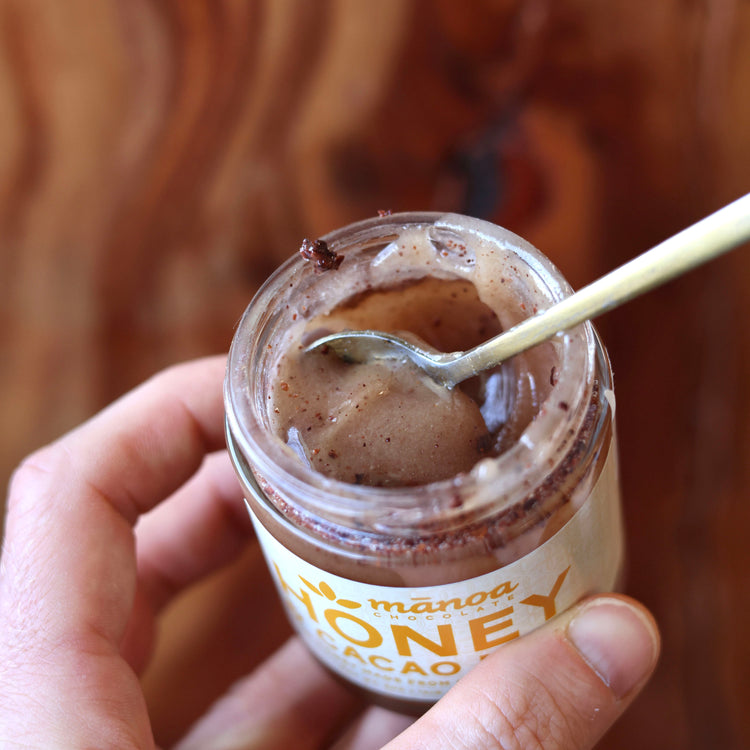 Hand holding a jar of honey cacao nibs  with a spoon